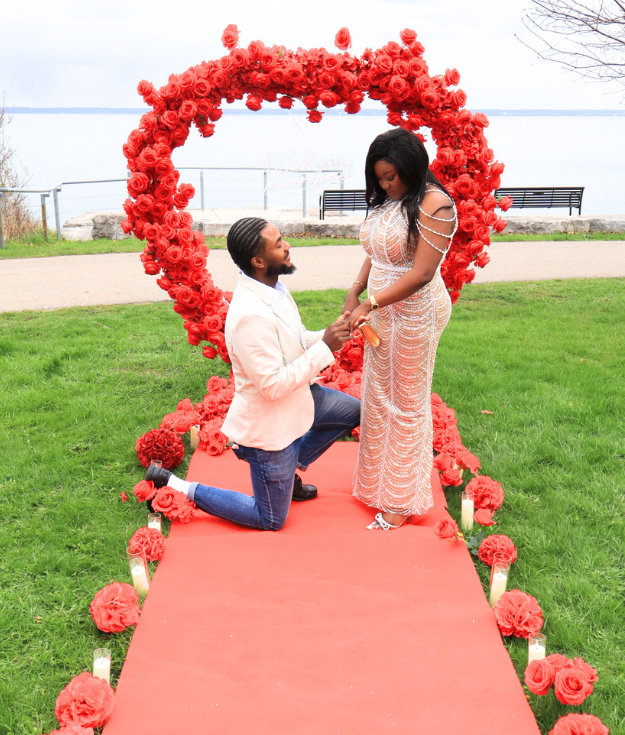 Romantic wedding proposal setup with flower wall, candles, and “Will You Marry Me” sign