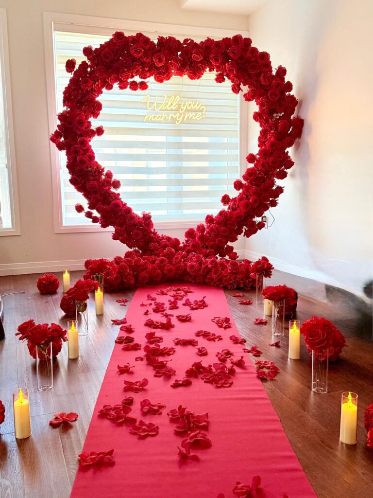 Romantic proposal setup featuring a white flower wall backdrop with candles, rose petals, and custom signage — perfect for engagements in Vaughan and the GTA.