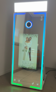 A state-of-the-art mirror photo booth with a vibrant interface displaying "Tap to Start!" and social sharing options, surrounded by a festive party scene.